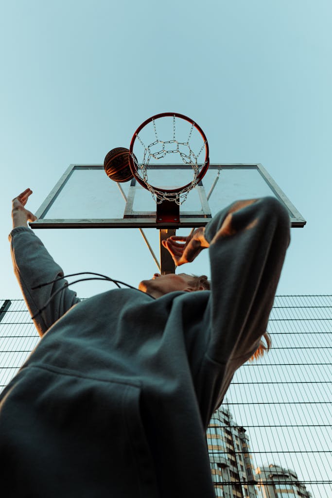 Dynamic low-angle shot of a basketball player shooting a hoop outdoors in an urban environment.